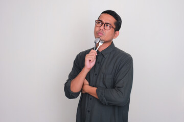 Adult Asian man thinking something while holding a spoon and fork