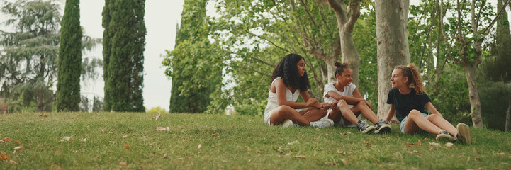 Three girls friends pre-teenage sit on the grass in the park and emotionally talking. Three teenagers on the outdoors