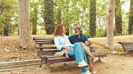 Happy couple talking while sitting on bench outside in the park in autumn