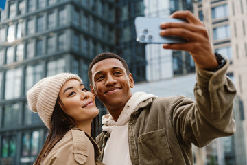 Beautiful couple taking selfies with smartphone camera and smiling while standing at street