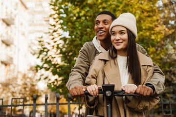 Beautiful couple smiling while riding electric scooter in park - obrazy, fototapety, plakaty