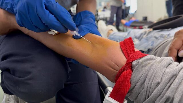 Paramedic's hands (in blue gloves) place cannula on patient's arm during military training course to become a combat paramedic. War in Ukraine