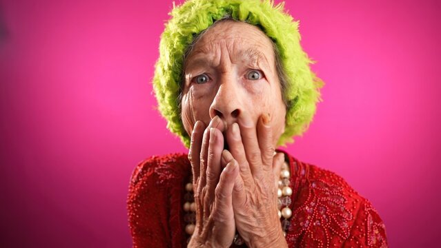 Happy fisheye portrait caricature of funny elderly woman with winner gesture having great success with green hat isolated on pink background.