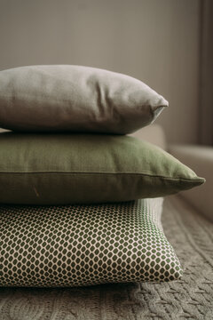 A stack of three IKEA pillows on a sofa. One pillow is gray, the second is green, the third is white with green polka dots. Brown IKEA blanket on the sofa