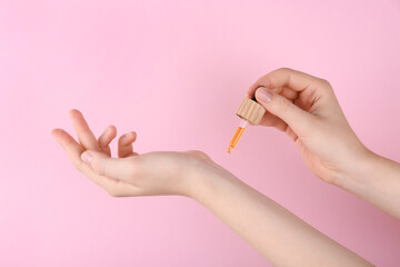 Woman applying essential oil onto wrist against pink background, closeup