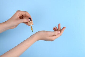 Woman applying essential oil onto wrist against light blue background, closeup