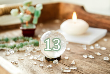 Number thirteen on Gemstone sphere or crystal balls known as crystallum orbis and orbuculum. Natural clear quartz ball on stand on wood tray in home. Predictions concept.