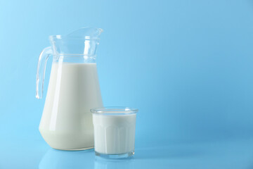 Jug and glass of fresh milk on light blue background, space for text