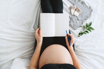 Pregnant woman with beautiful belly makes notes or check list in paper diary.