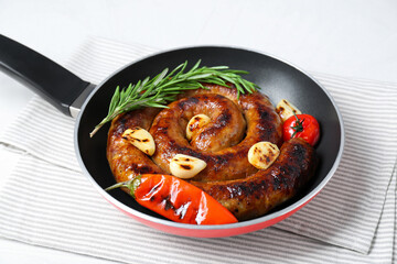 Delicious homemade sausage with garlic, tomato, rosemary and chili in frying pan on table, closeup