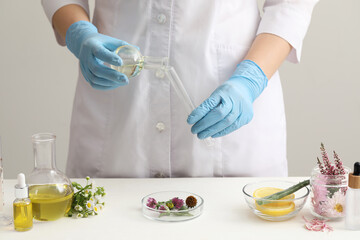 Scientist developing cosmetic oil at white table, closeup