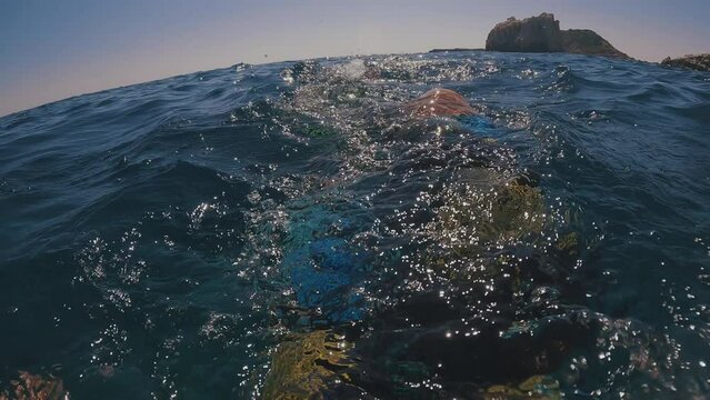 POV shot, guy paddling with his fins underwater next to beautiful rocky shore