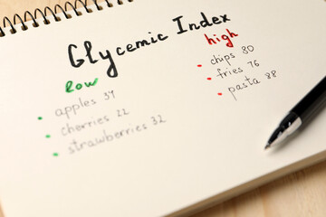 List with products of low and high glycemic index in notebook and pen on table, closeup