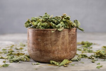 Bowl with dry parsley on light grey textured table, closeup