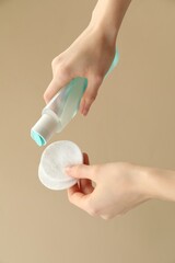 Woman pouring makeup remover onto cotton pads on beige background, closeup