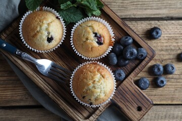 Delicious sweet muffins with blueberries, mint and fork on wooden table, flat lay