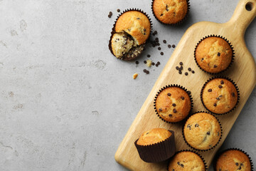 Delicious sweet muffins with chocolate chips on grey textured table, flat lay. Space for text