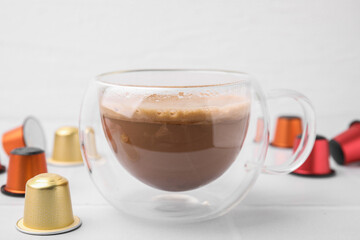 Cup of coffee and capsules on white table, closeup