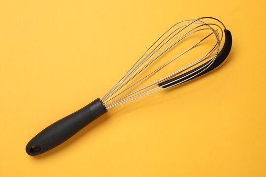 Metal whisk on yellow background, top view. Kitchen tool