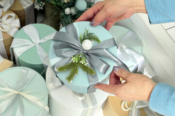 Women's hands hold in their hands a round box of pale blue color with a Christmas gift on the background of other gifts