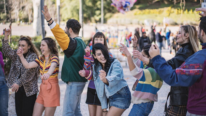 Group of joyful young friends dancing and celebrating in an urban park, enjoying a sunny day...