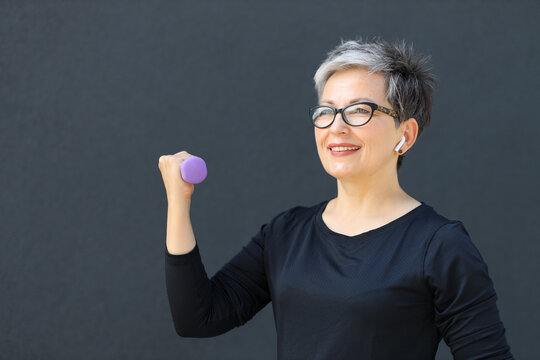 Happy mature Caucasian woman enjoys fitness, lifting dumbbells outdoors, radiating health, and cheerfulness in her 60s.
