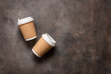 Coffee in paper cups lay flat on a dark brown background. View from above. Disposable tableware....
