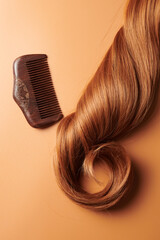 Curls of brown hair and a wooden comb on an orange background, hair care, beauty salon concept