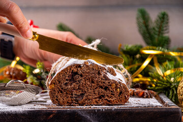 Homemade Christmas chocolate stollen. Traditional december holiday, New Year and Christmas baked sweet dessert, dark chocolate pastry with dried fruit and nuts, on cozy Xmas decorated background