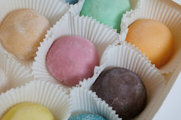 White plastic box with Japanese rice desert mochi closeup. Colouful mochi cakes sliced. Tasty fruit and chocolate mochi on grey background. Traditional cold ice asian candy. Dry fruits and nuts.