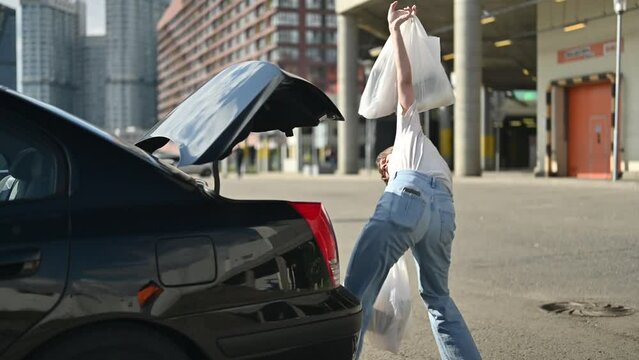 A comical depiction of how inconvenient it is to load shopping bags into an old sedan. Young woman with busy hands trying to load her shopping into car