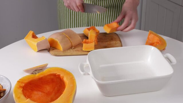 hands slice butternut pumpkin in baking dish