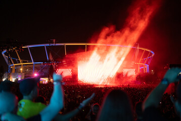 Neon fire-like stage lights show at a concert. Audience partying and dancing