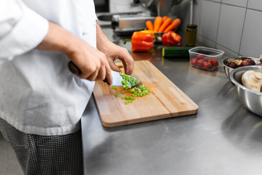 cooking food, profession and people concept - close up of male chef with knife chopping celery on cutting board at restaurant kitchen