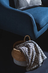 interior and home decor concept - close up of blue chair with pillow and blanket in basket over black wall