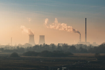 Landscape with field and trees, in the distance factory and a power station, with the factory pipes...