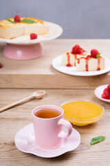 Colorful breakfast. Tea in a pink mug and dessert with raspberries on a light wooden table