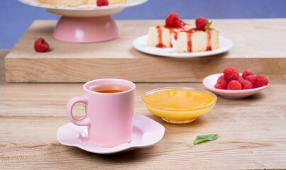 Colorful breakfast. Tea in a pink mug and dessert with raspberries on a light wooden table
