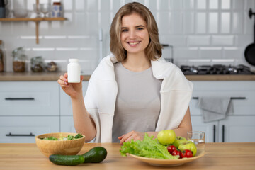 Smiling young caucasian woman holding bottle of dietary supplements or vitamins in her hands. Healthy lifestyle concept