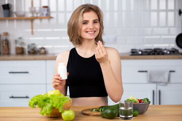 Beauty supplement. Attractive young woman holding vitamin capsule and glass of  water  at the...