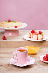 Colorful breakfast. Tea in a pink mug and dessert with raspberries on a light wooden table