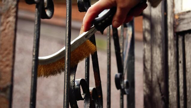 Homeowner cleaning rusty wrought iron fence with wire brush