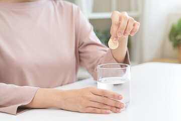 Close up young woman hand putting or dropping effervescent tablet into glass of water, holding pain...