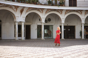 Young, beautiful, blonde American woman in a red dress with white polka dots, walking in the square...