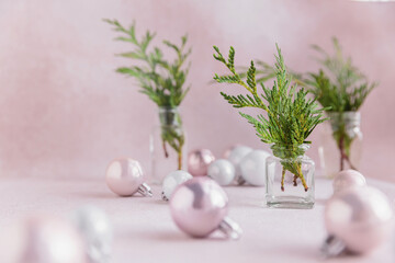 Still life from Cypress branches in transparent vases with Christmas decorations. Bouquet with evergreen spruce and balls on light pink background. Minimalist Christmas decor in in pastel colors