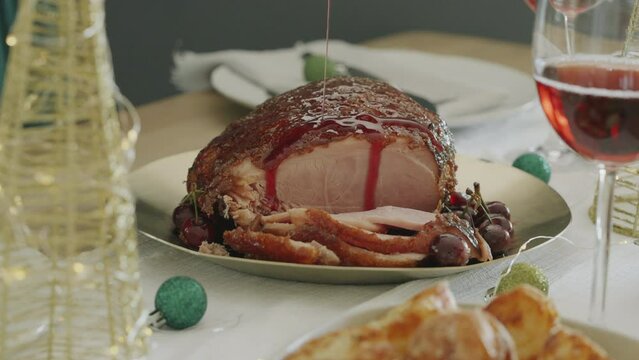 Medium close-up clip of a Christmas Gammon on a decorated xmas dinner or lunch table. Sliced glazed ham and beautiful woman pouring cherry glaze over the meal. Home cooked festive family meal.