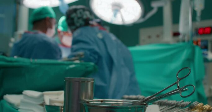 Blurred unrecognizable shot of hospital staff performing surgery in operating room. Surgical instruments on table in operating theatre. Hospital lamp illuminate surgeon and nurses