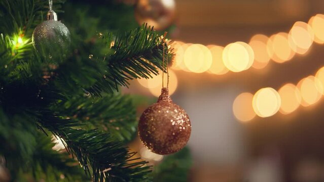 Close-up hand of woman decorating Christmas tree with baubles balls on the background of festive lights at home on calm winter evening, Christmas and new year concept, vertical view orientation
