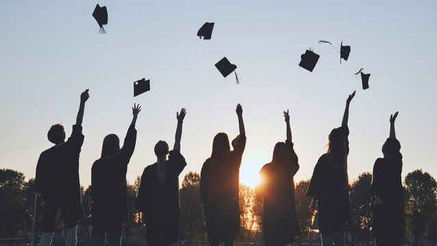 Silhouettes of Happy college graduates tossing their caps up at sunset.