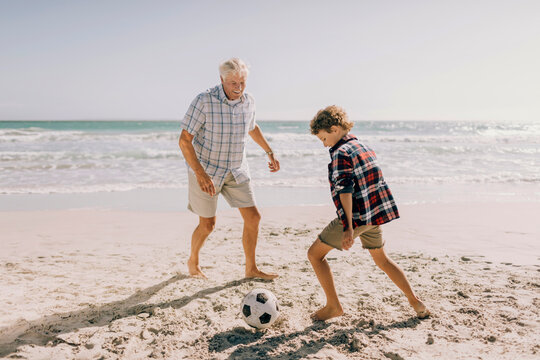 Grandfather and grandson playing soccer on sandy summer beach